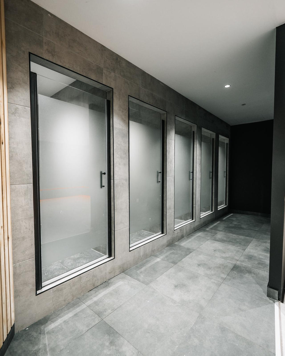 Shower cubicles with frosted glass doors and dark tiled walls
